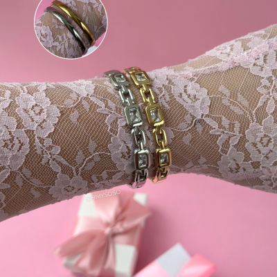 Pulseiras metálicas prateada e dourada com pedras sobre pulso com renda rosa e fundo rosa.