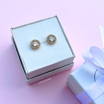 Brincos redondos com pedras numa caixa branca sobre fundo rosa e caixa de presente ao lado