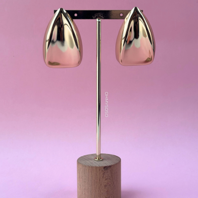 Brincos dourados em suporte de madeira com fundo rosa