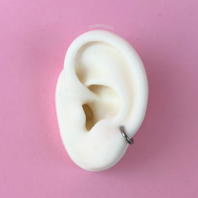 Molde branco de orelha com anel prateado sobre fundo rosa