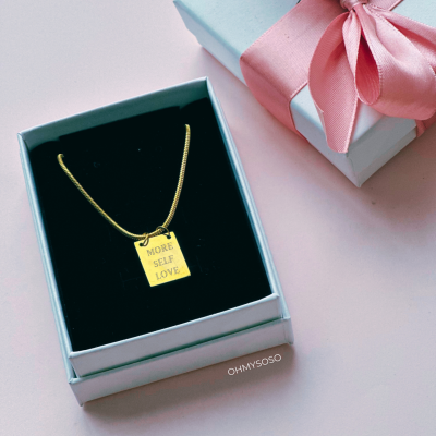 Colar dourado com pendente retangular e caixa de presente branca com fita rosa