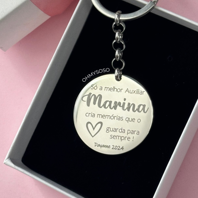 Chaveiro redondo prateado com gravação personalizada dentro de caixa preta e branca sobre fundo rosa