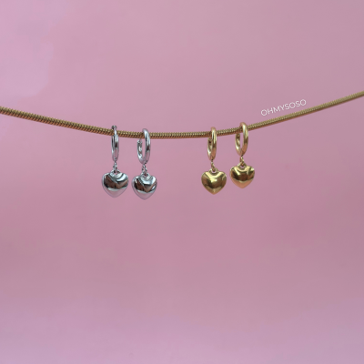 Brincos de coração prateados e dourados pendurados num fio dourado sobre fundo rosa