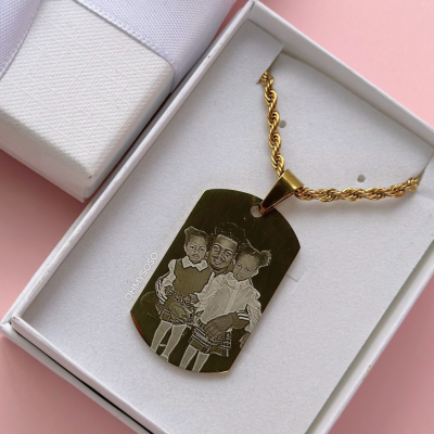 Colar dourado com pendente gravado numa caixa branca com laço branco e fundo rosa