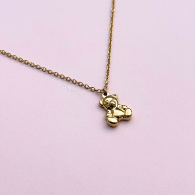 Colar com pendente dourado em forma de urso sobre fundo rosa claro