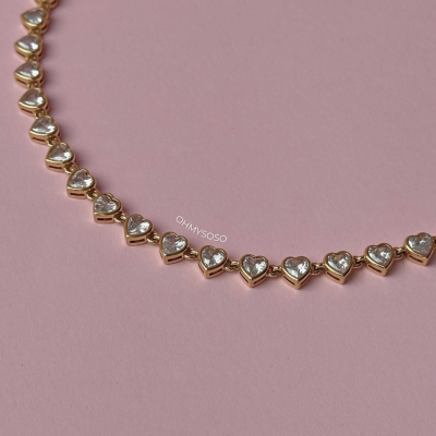 Colar de corações dourados com pedras transparentes sobre fundo rosa