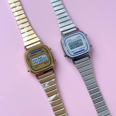 Relógios digitais dourado e prateado com braceletes metálicas sobre fundo rosa