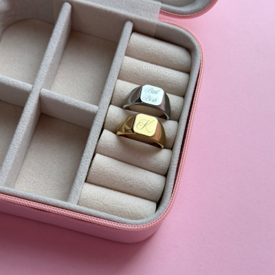 Estojo de veludo com dois anéis gravados, prateado e dourado, sobre fundo rosa