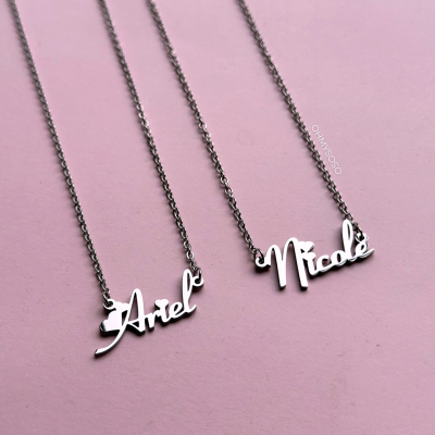Colares personalizados em metal prateado com os nomes Ariel e Nicole em fundo rosa.
