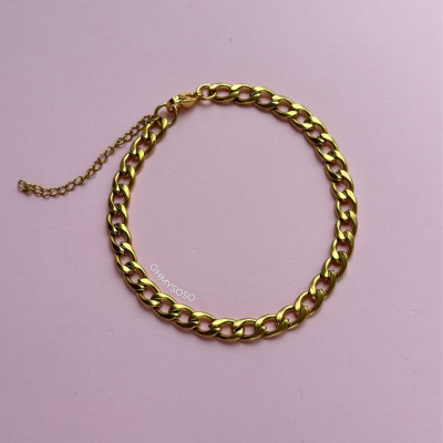 Pulseira dourada com elos grossos num fundo rosa claro