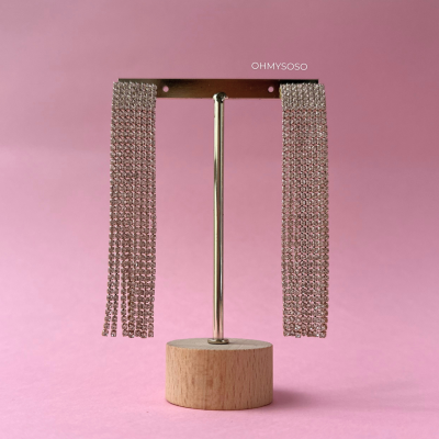 Brincos prateados compridos com correntes em suporte de madeira sobre fundo rosa