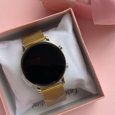Relógio inteligente dourado com mostrador preto dentro de caixa rosa e almofada branca