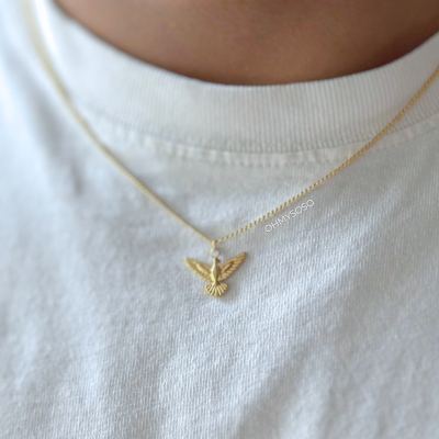 Colar dourado com pendente de pássaro sobre t-shirt branca