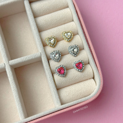 Brincos de coração brilhantes organizados numa caixa de veludo bege com borda rosa