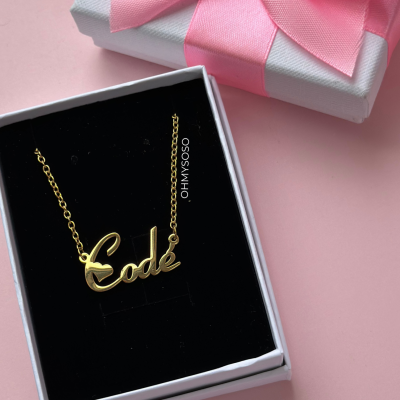 Colar dourado com pendente 'Codé' numa caixa preta dentro de caixa branca com laço rosa