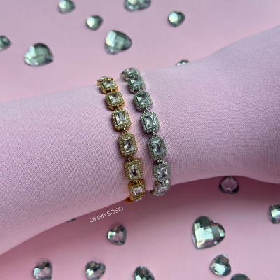 Duas pulseiras brilhantes, dourada e prateada, com pedras retangulares sobre fundo rosa com corações facetados