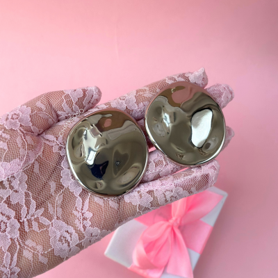 Mãos com luvas de renda seguram brincos prateados redondos ondulados e caixa de presente rosa e branca