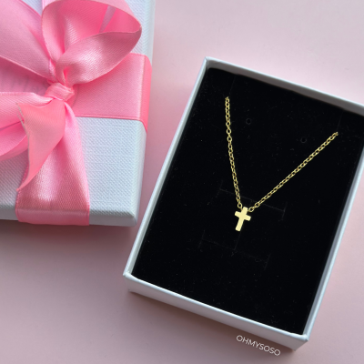 Colar dourado com pingente de cruz em caixa preta, com caixa branca e fita rosa ao lado