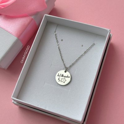 Colar prateado com pendente redondo gravado em caixa branca com laço rosa