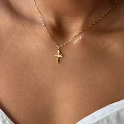 Colar dourado com pendente de cruz estilizada no pescoço de uma pessoa com roupa branca