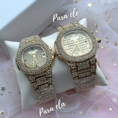 Dois relógios dourados com pedras brilhantes sobre almofada branca e tecido rosa com estrelas.