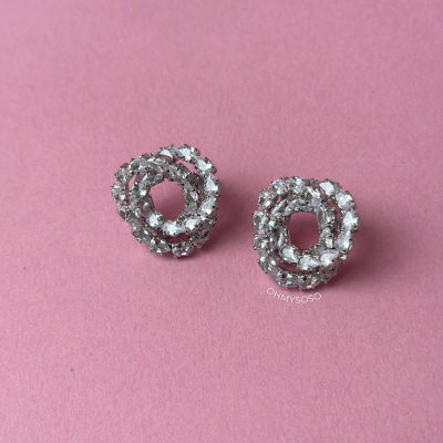 Brincos redondos prateados com pedras transparentes brilhantes sobre fundo rosa