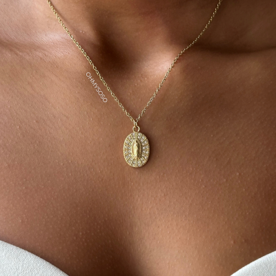 Colar dourado com pendente oval e pedras brilhantes ao pescoço.