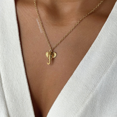 Colar dourado com pendente cabeça de elefante em pescoço feminino com casaco branco canalé