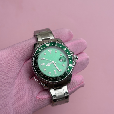 Relógio de pulso com mostrador verde e bracelete metálica prateada sobre fundo rosa