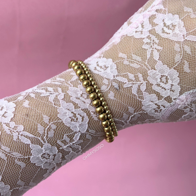 Braço com meia-calça de renda branca e pulseiras douradas sobre fundo cor de rosa