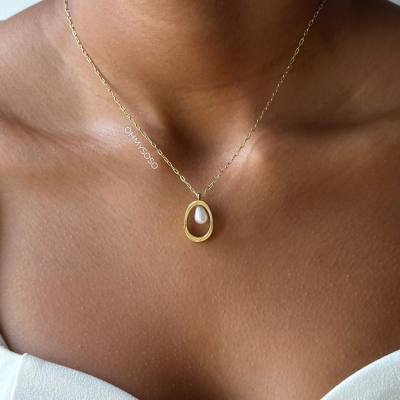 Colar dourado com pendente oval e pérola no pescoço de mulher com vestido branco