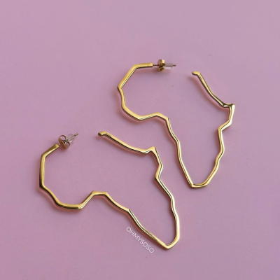 Brincos dourados em formato do continente africano sobre fundo rosa claro