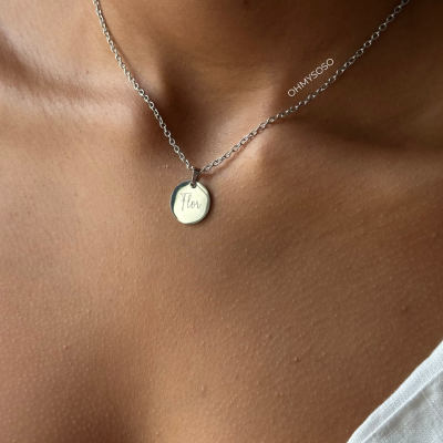 Colar prateado com pendente circular e texto Flor ao pescoço