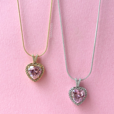 Dois colares com pendentes em forma de coração e pedras cor-de-rosa sobre fundo rosa