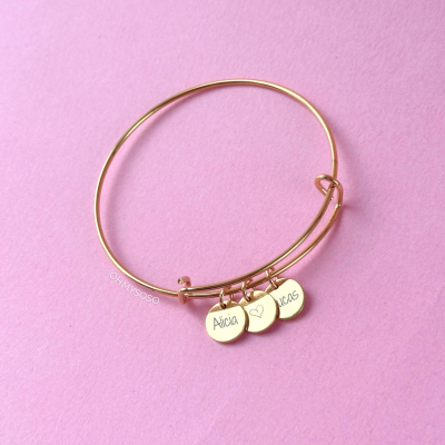 Pulseira dourada com três pendentes com nomes Alicia, coração e Lucas em fundo rosa