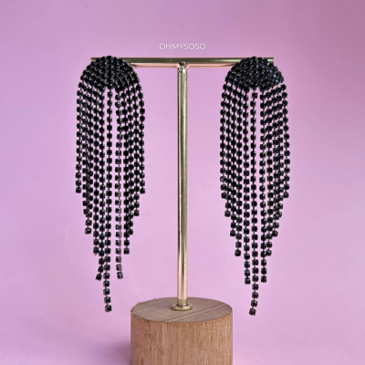 Brincos pendentes pretos em suporte dourado com base de madeira em fundo rosa