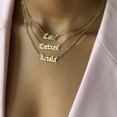 Três colares dourados com pendentes em letra gótica usados ao pescoço