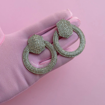 Brincos de argola com cristais brilhantes segurados por mão com luva rosa