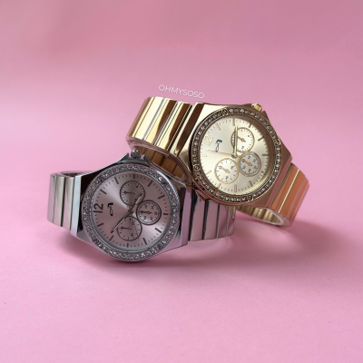 Dois relógios metálicos, prateado e dourado, sobre fundo rosa