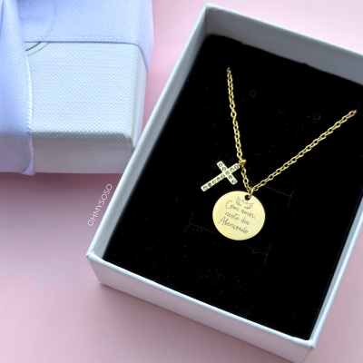 Colar dourado com pendentes redondo e cruz numa caixa branca com interior preto
