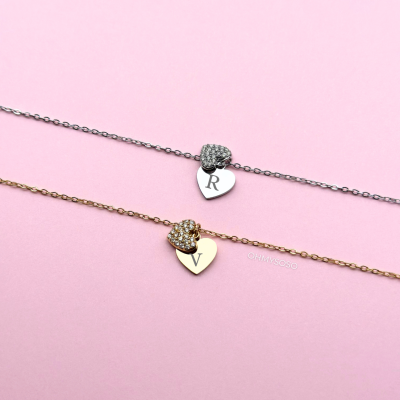 Duas pulseiras com medalhas de coração e letras R e V em fundo rosa