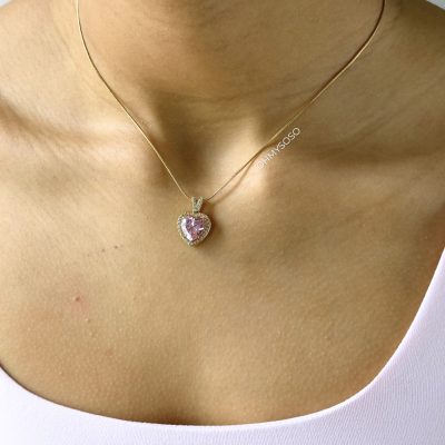 Colar com pendente em forma de coração com pedra rosa e corrente dourada no pescoço
