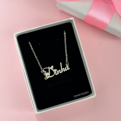 Colar com pendente a palavra Dinha em prata numa caixa preta e branca, com caixa prateada e laço rosa ao lado