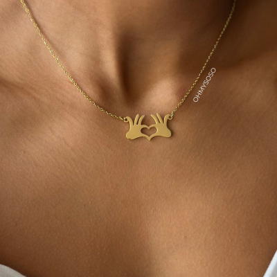 Colar dourado com pendente de mãos formando coração no pescoço.