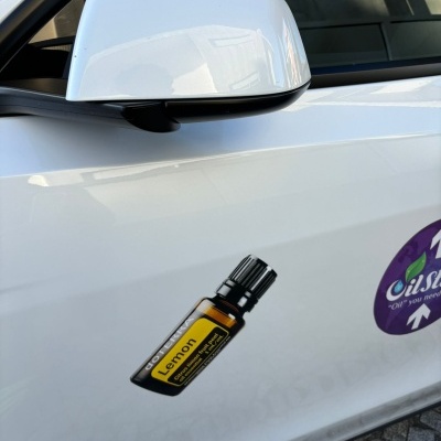 Lado do carro branco com duas etiquetas adesivas, uma mostrando um frasco de óleo essencial Lemon.
