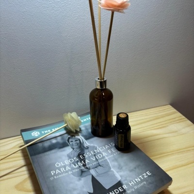 Frasco de vidro castanho com sticks e flores artificiais e livro com óleo essencial numa mesa de madeira