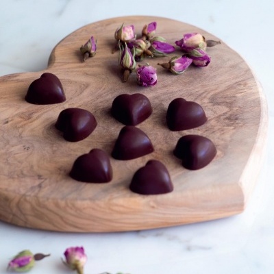 Bombons em forma de coração e botões secos de rosa sobre tabuleiro de madeira em forma de coração