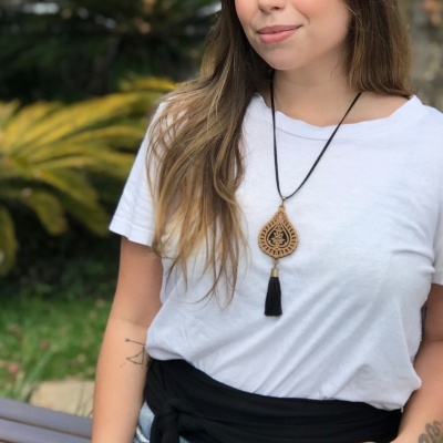 Mulher a usar colar pendente em madeira com tassel preto, t-shirt branca e casaco preto