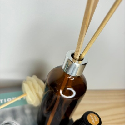 Frasco âmbar para difusor com palitos de madeira e óleo essencial ao lado sobre mesa de madeira