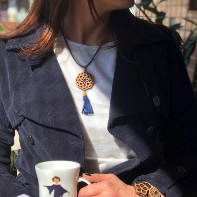 Colar e anel de madeira com tessel azul usados por pessoa com casaco azul a segurar caneca.